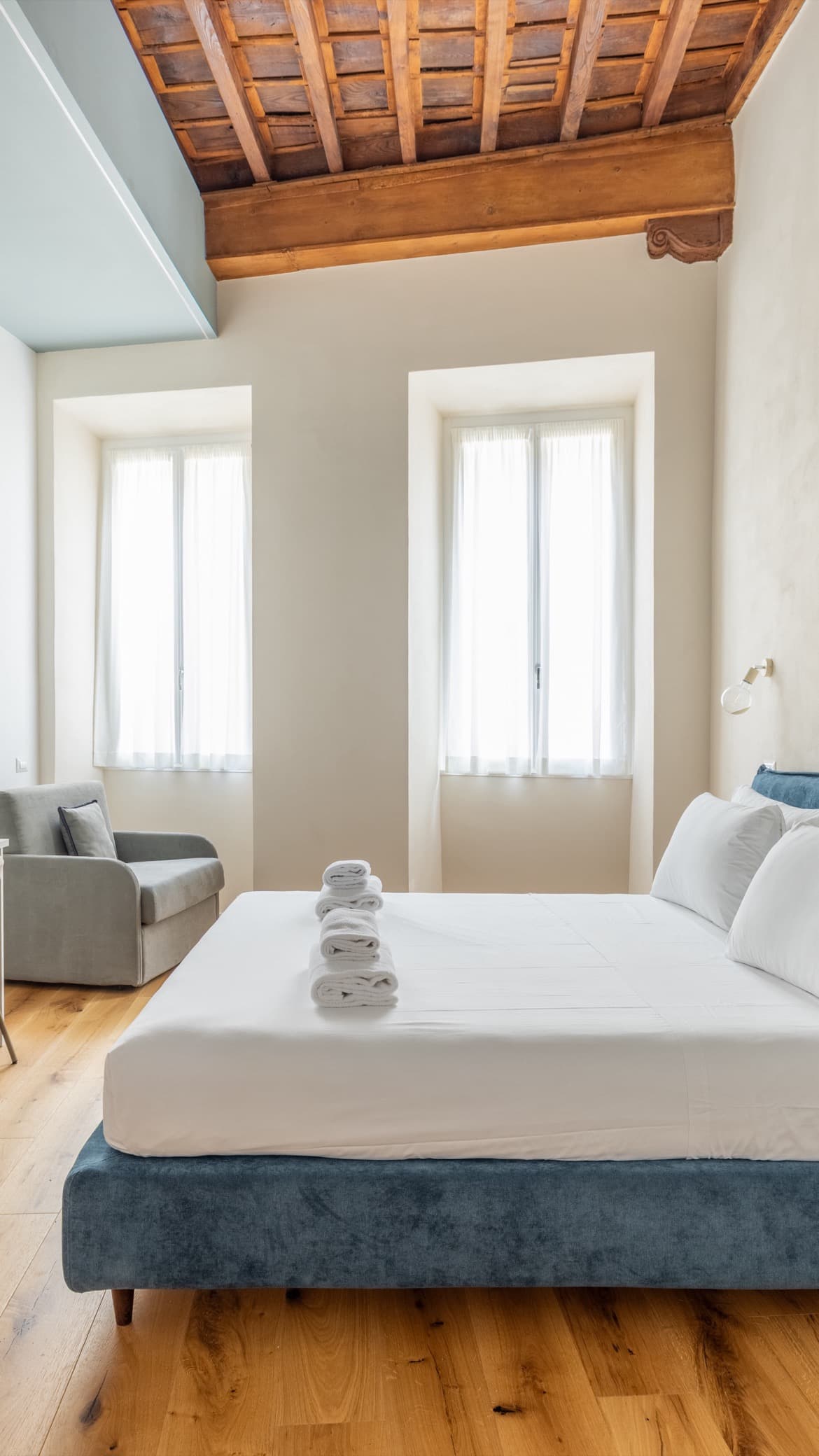 Camera da letto luminosa con travi a vista e biancheria fresca in un appartamento gestito da Serenia a Roma
